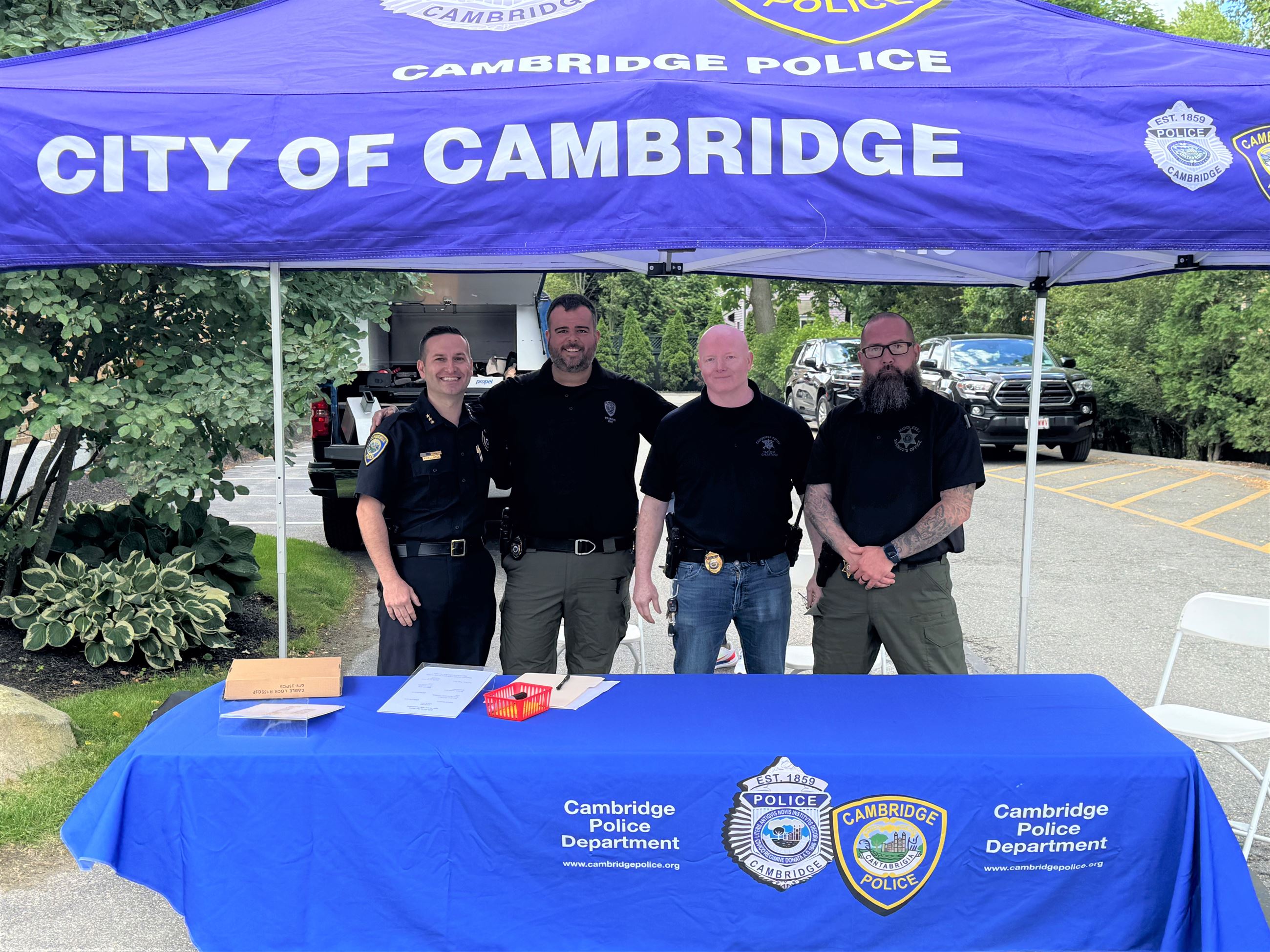 Four individuals standing behind a table at a Cambridge Gun Buyback event